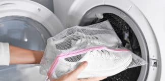 Woman putting mesh with white sneakers into washing machine, closeup